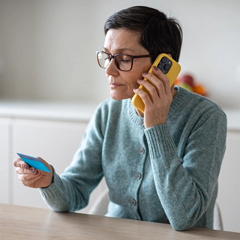 Photo of an older woman holding a credit card and listening to a phone.